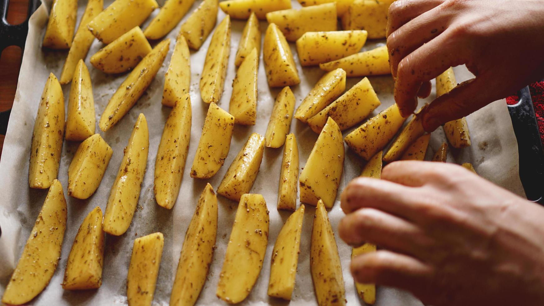 manos - patatas crudas en rodajas en una bandeja para hornear foto