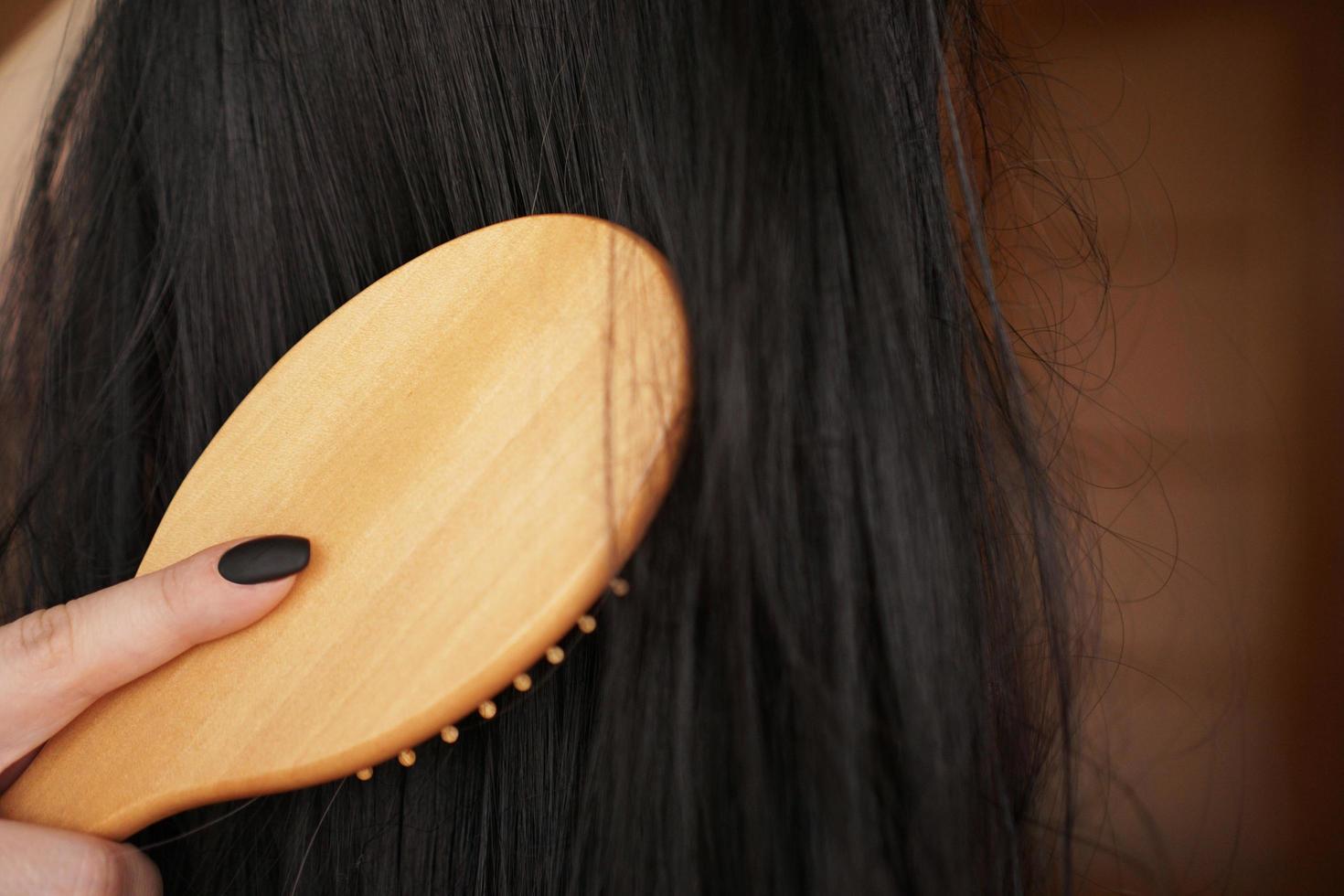 Female hand holds a black wig with long hair and combs a wooden comb photo