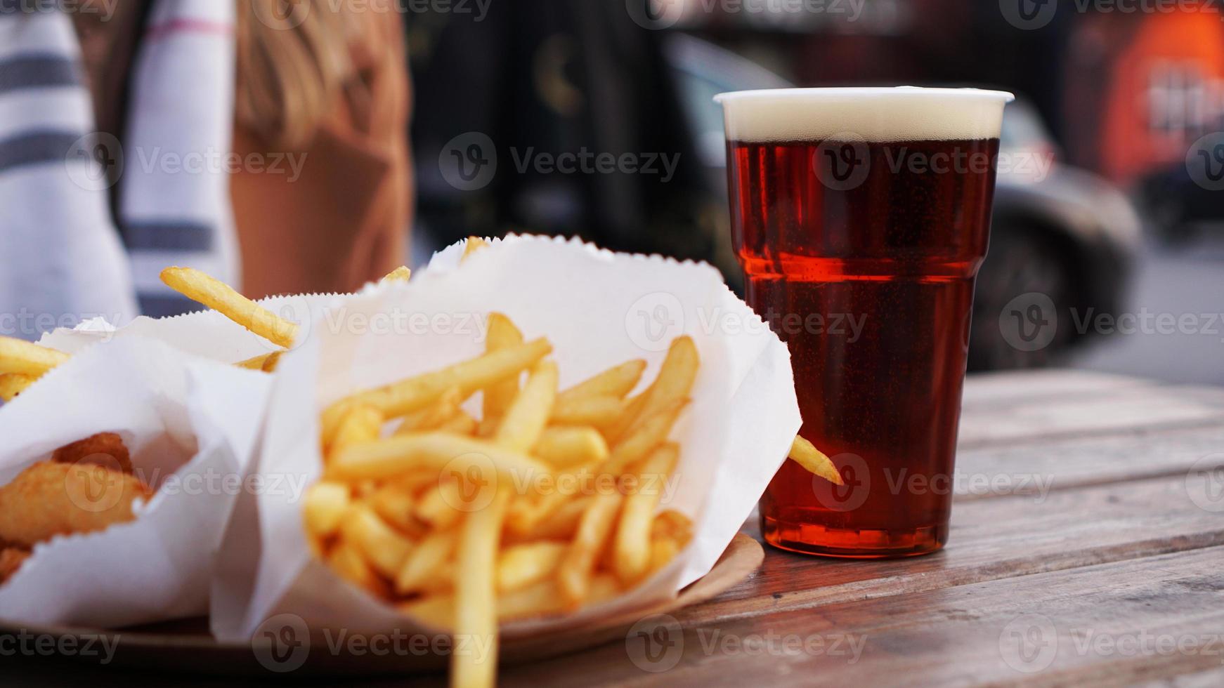 cerveza oscura y papas fritas en una mesa de madera. zona de comidas. comida para llevar foto