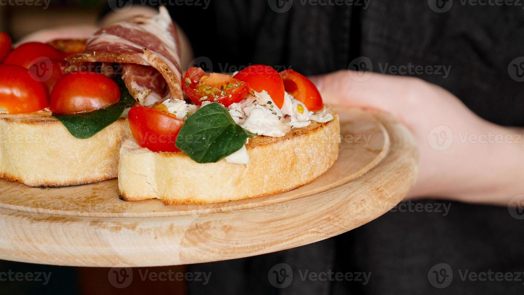 Mujer camarero sosteniendo una bandeja de madera con bruschetta en la mano foto