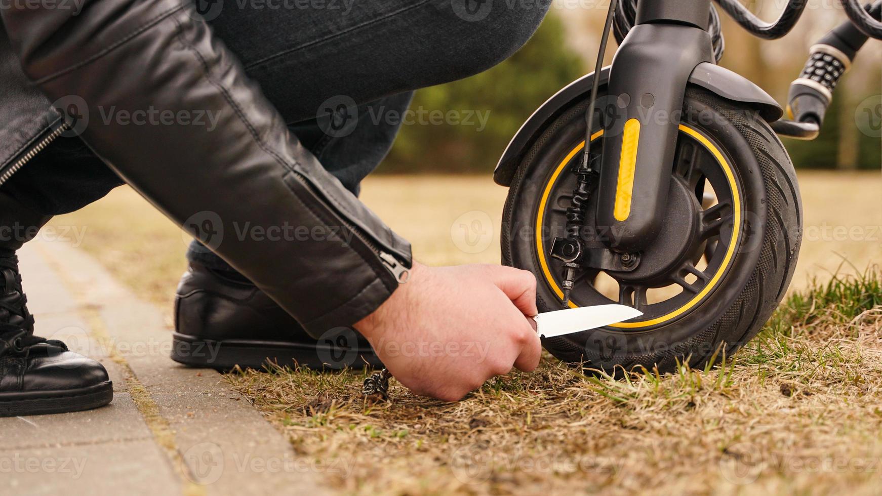 A man's hand is cutting the tire of an electric scooter with a knife. photo