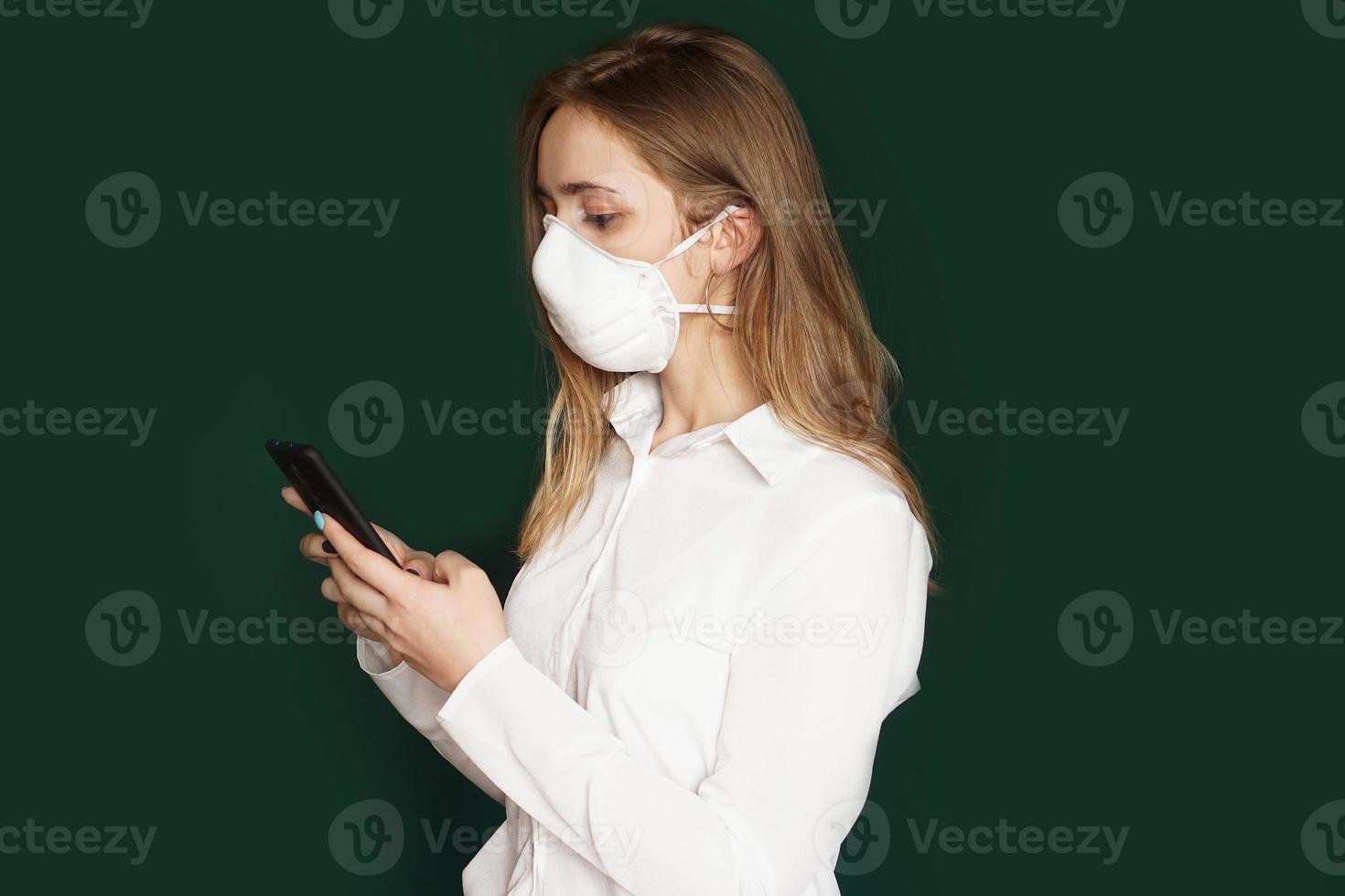 Girl in a medical mask with phone in hands on a green background photo