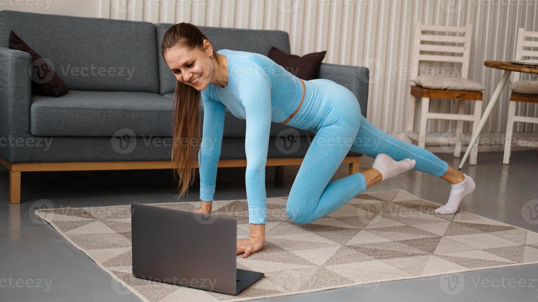Hermosa joven haciendo ejercicio físico en casa con su computadora portátil foto