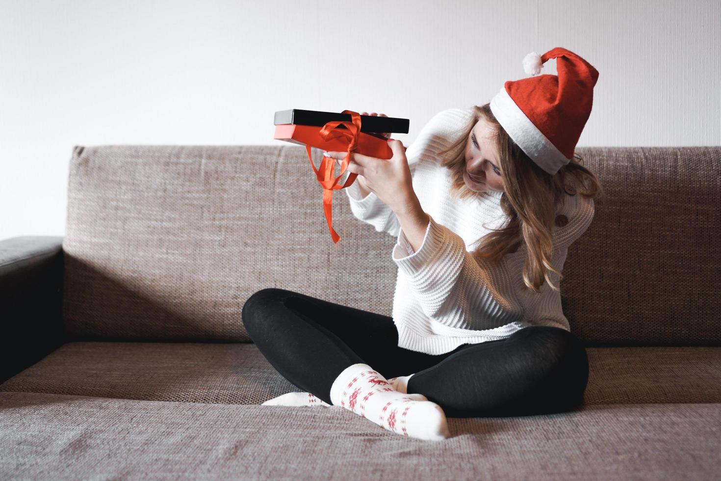 Beauty girl opening present gifts sitting on sofa at home photo