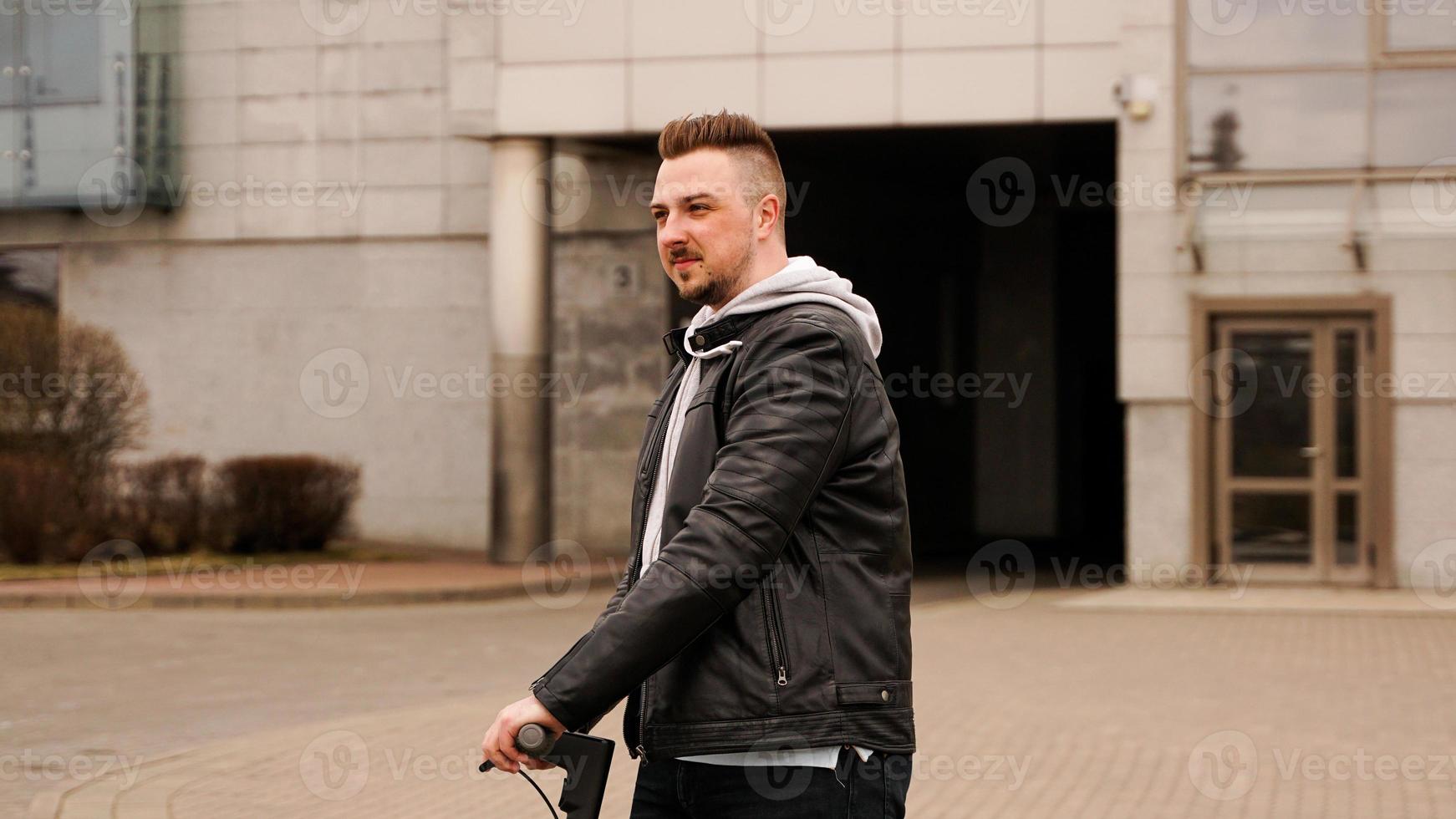 Tall man on an electric scooter against gray city buildings photo