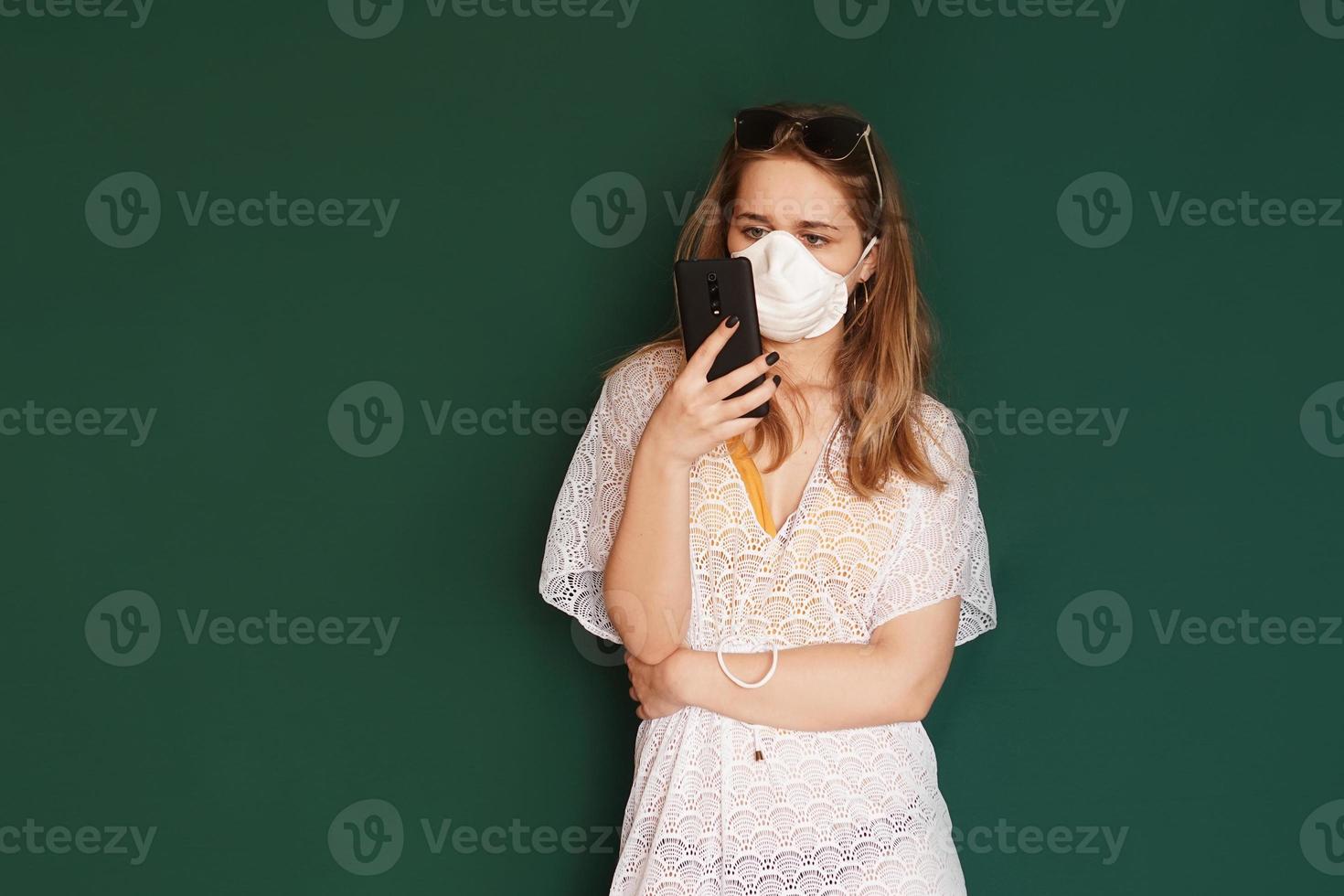 turista niña en una máscara médica con teléfono en manos en un verde foto