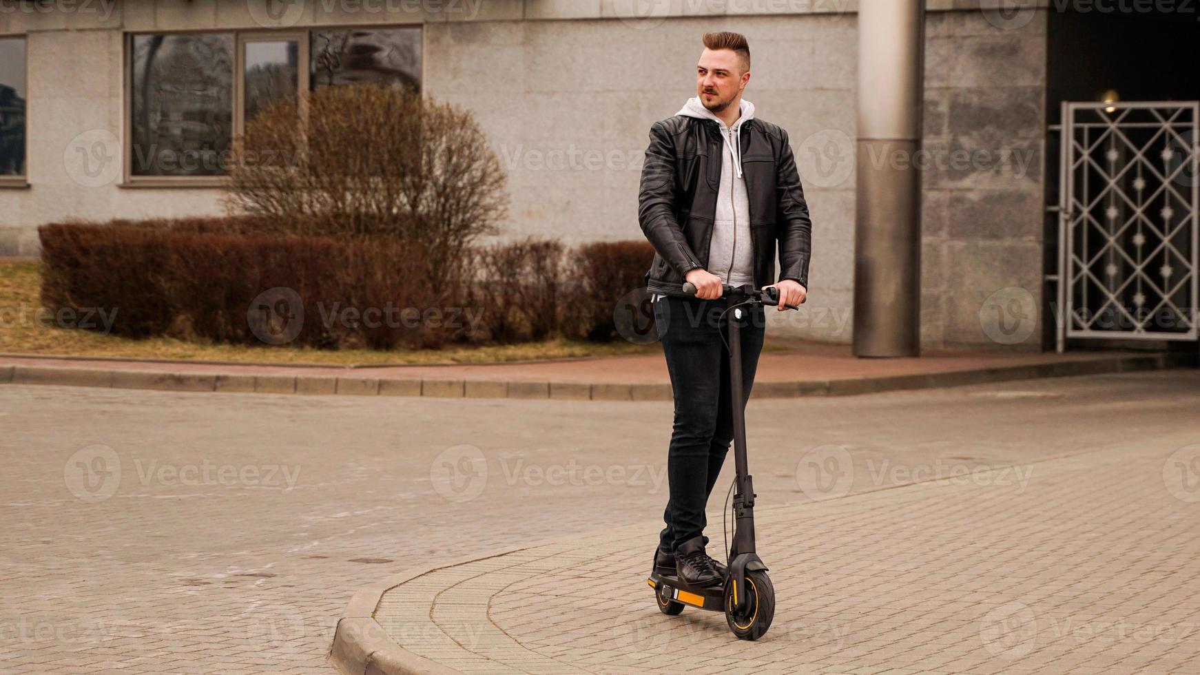 Hombre alto en un scooter eléctrico contra los edificios de la ciudad gris foto