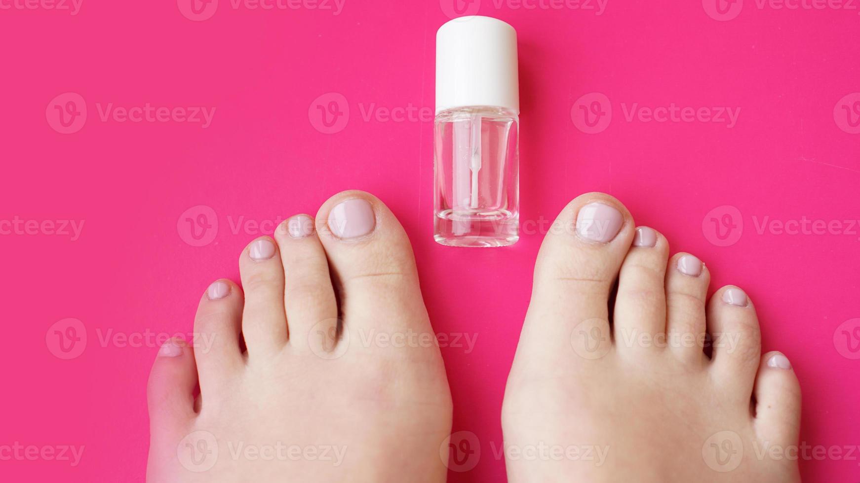 Pedicure with transparent nail polish on pink background photo