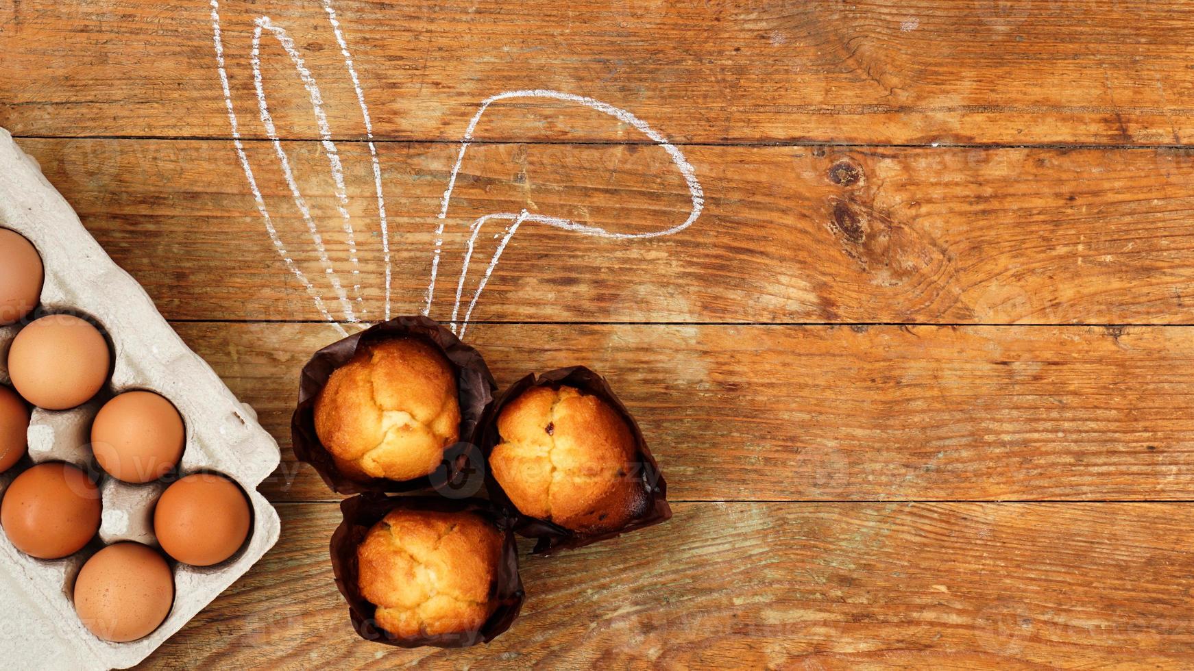 Homemade muffin with painted rabbit ears. Muffin and eggs on a wooden photo