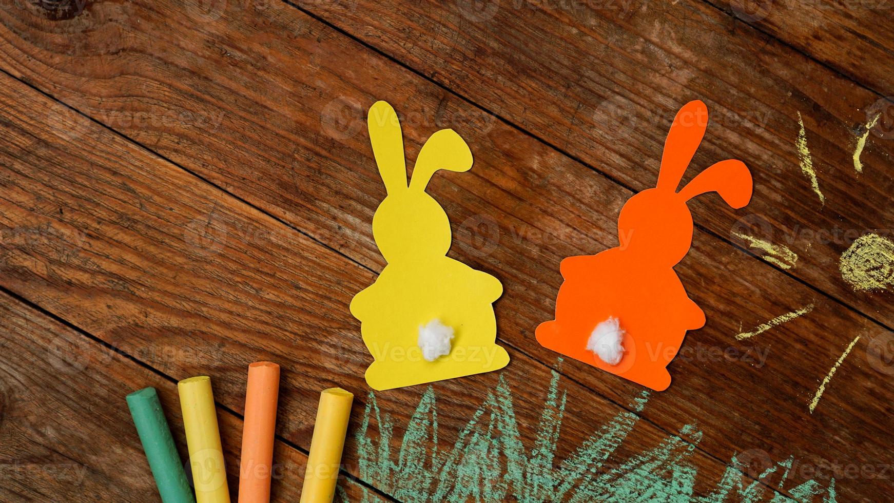 Two Easter bunnies made of paper. Drawn with colored chalk grass photo