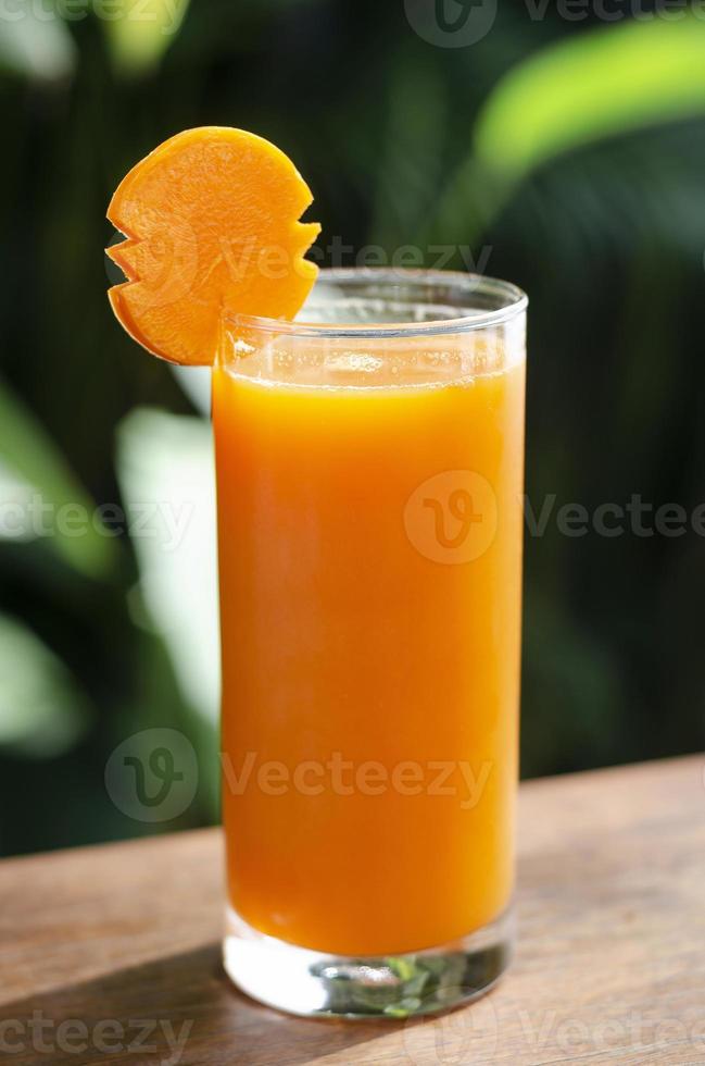 Vaso de jugo de zanahoria orgánico fresco en la mesa al aire libre en la mesa en el soleado jardín al aire libre foto