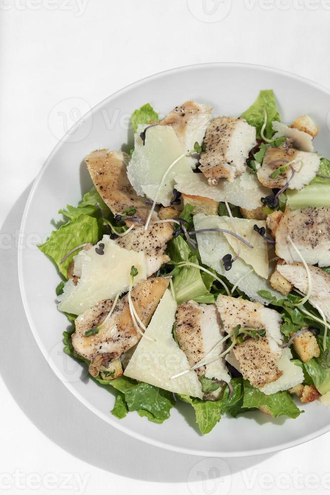 Organic chicken caesar salad with parmesan cheese and croutons on white table background photo