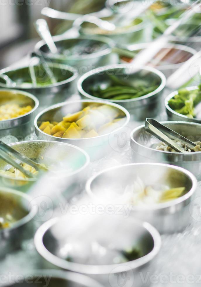 Bowls of mixed fresh organic red peppers and vegetables in modern salad bar display photo