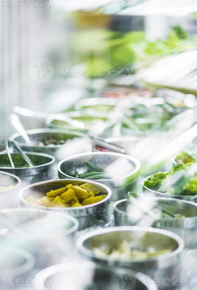 Bowls of mixed fresh organic red peppers and vegetables in modern salad bar display photo