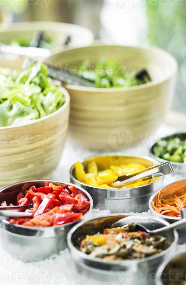 Bowls of mixed fresh organic red peppers and vegetables in modern salad bar display photo