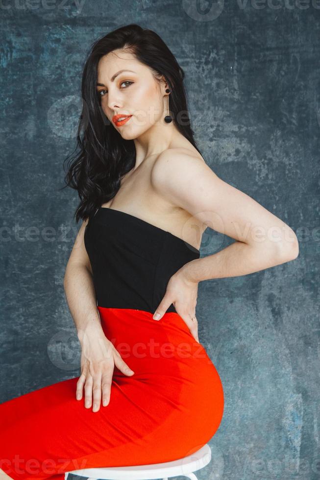 Mujer vistiendo un vestido rojo sentada en una silla sobre un fondo gris foto