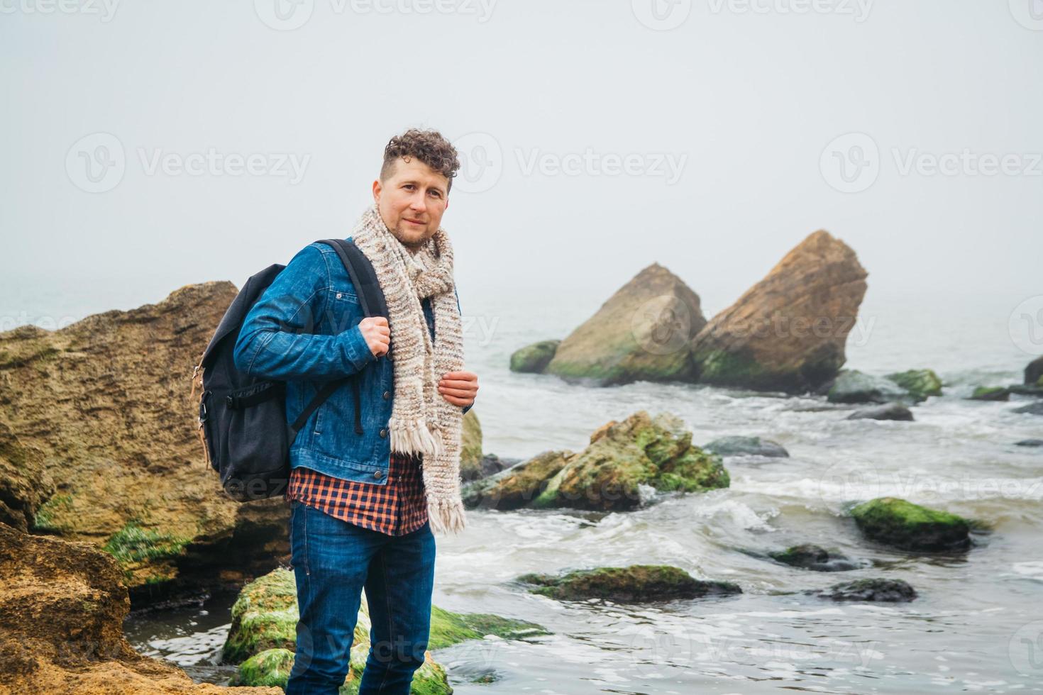 Hombre viajero con una mochila se encuentra en una roca frente a un hermoso mar foto