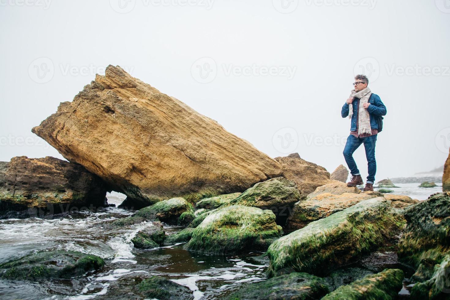 Traveler man with a backpack stands on a rock against a beautiful sea photo
