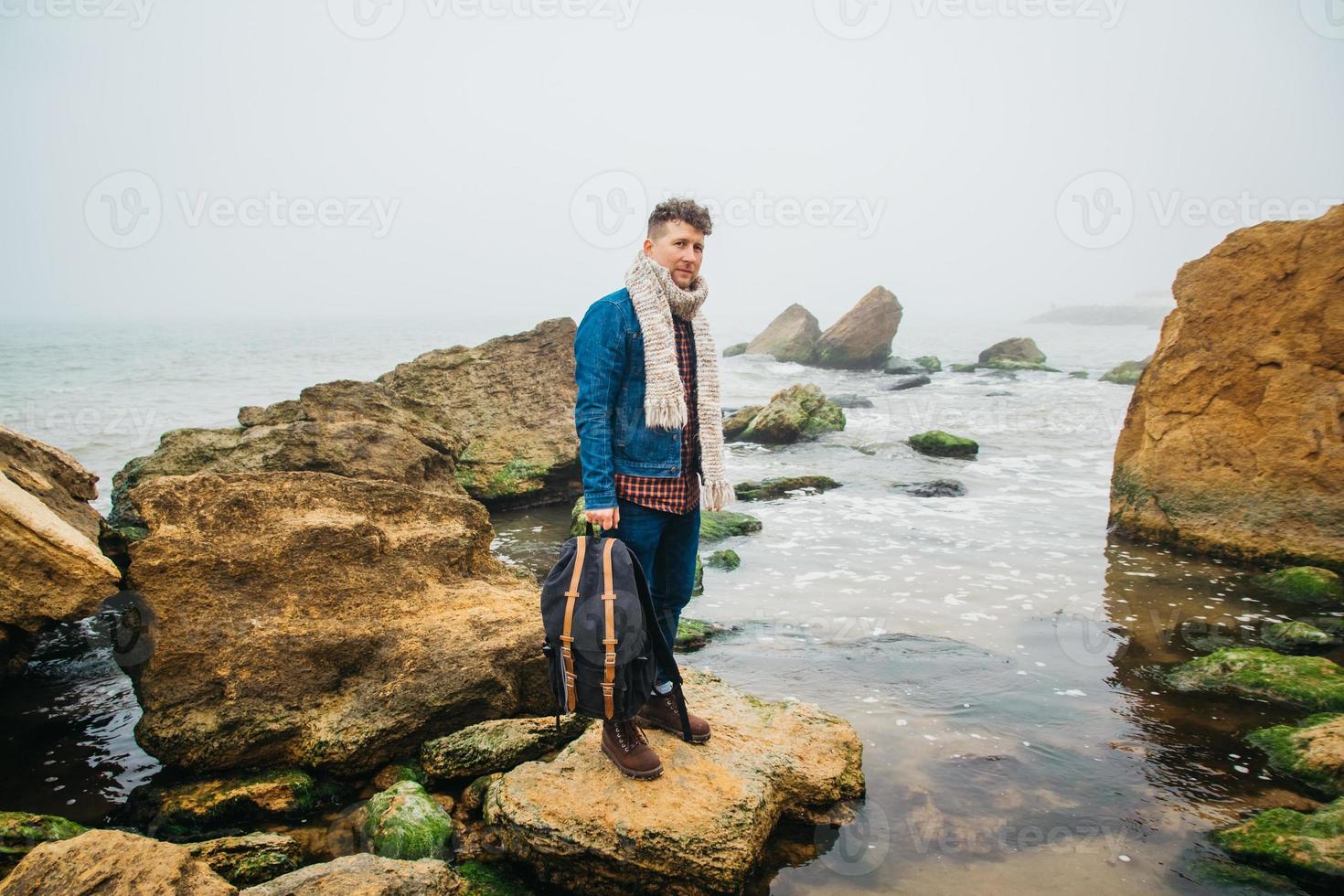 Hombre viajero con una mochila se encuentra en una roca frente a un hermoso mar foto