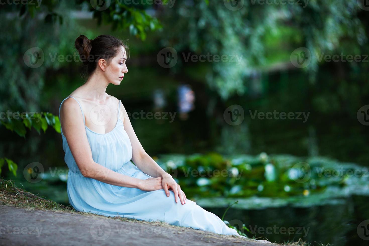 Sad young woman sits on the shore of the pond photo