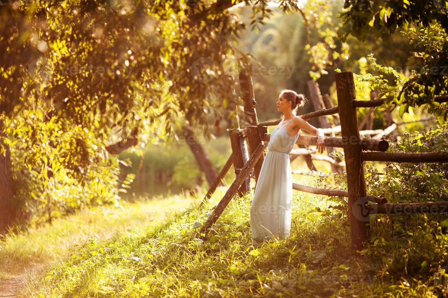 Young woman is leaning against the hedge in the evening in the garden photo