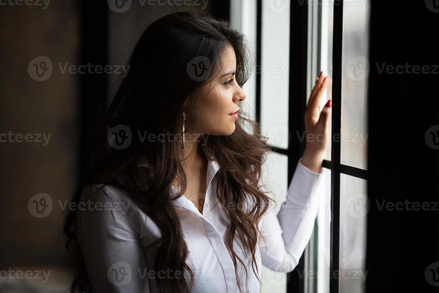 hermosa joven de pelo oscuro mira por la ventana foto