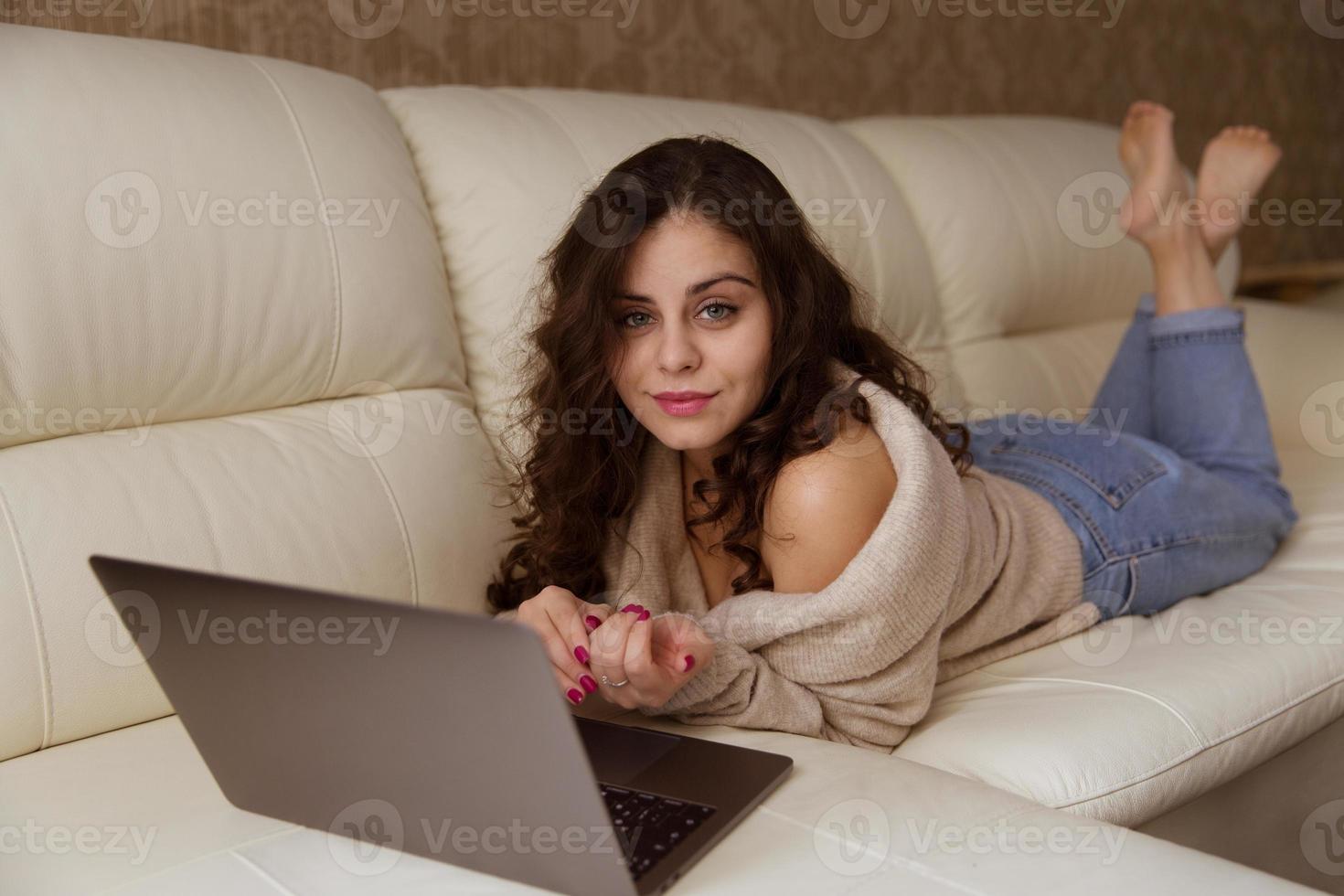 Woman is lying on the sofa with a small laptop photo