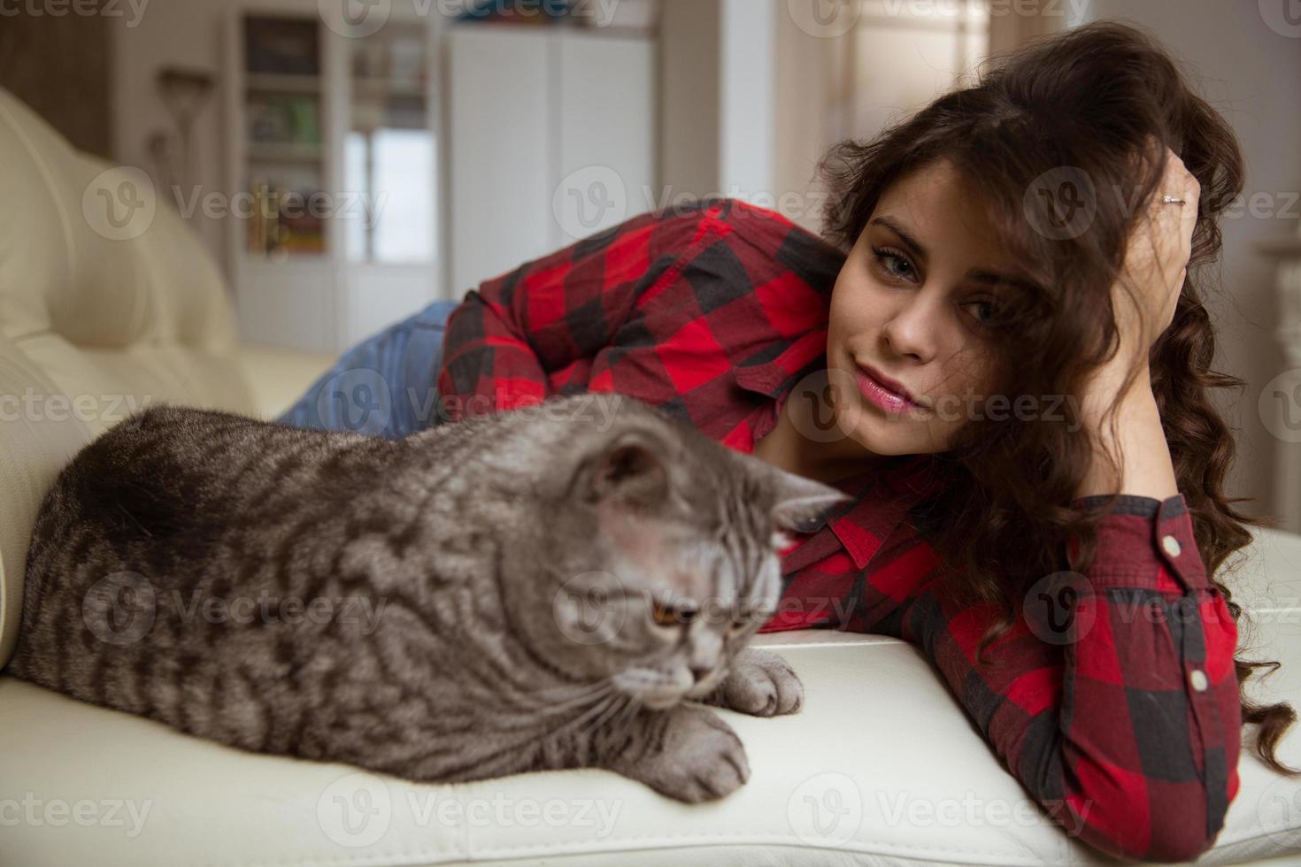 Beautiful woman is lying on the sofa with a big cat photo