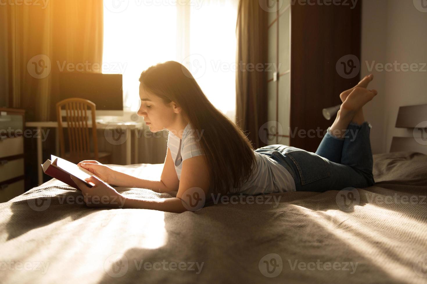 Girl is lying on the bed and reading a book photo