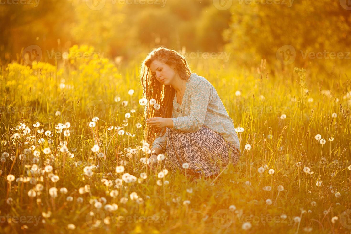 A girl with dreadlocks tearing dandelions in the middle of the meadow photo