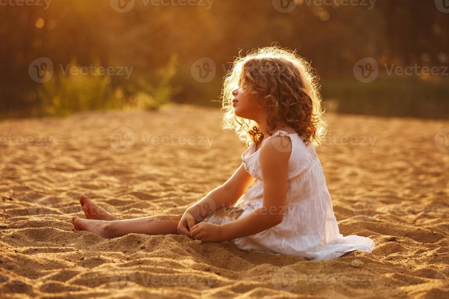 Little girl in dress sitting on the sand photo