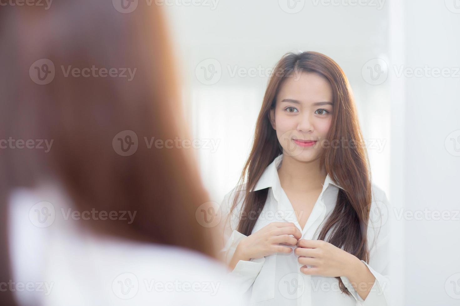 mujer asiática joven que examina con la cara y la sonrisa que miran en el espejo. foto