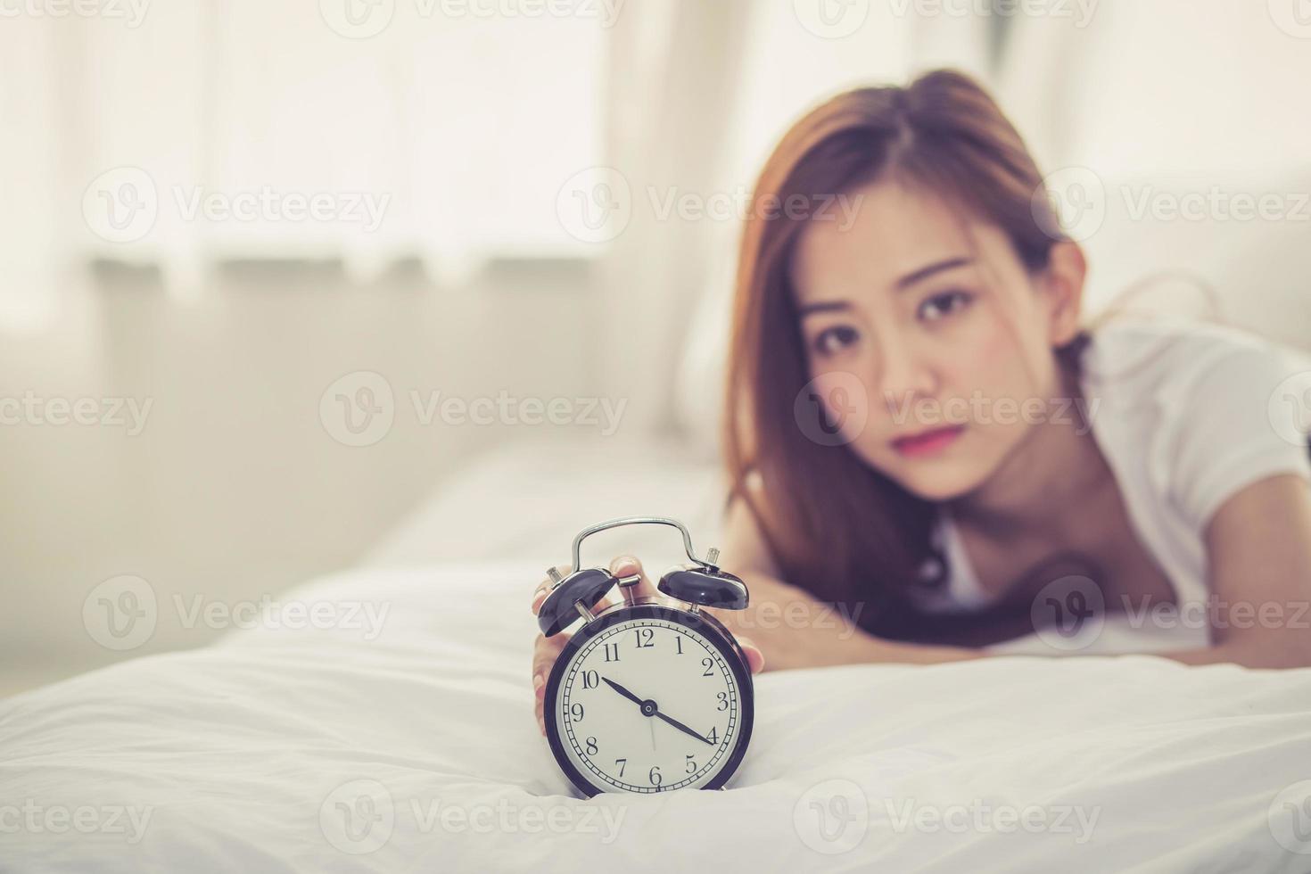 Young asian woman turn off alarm clock in good morning. photo