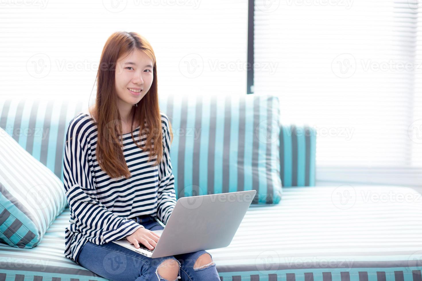 Young asian woman using laptop for leisure on sofa in living room. photo