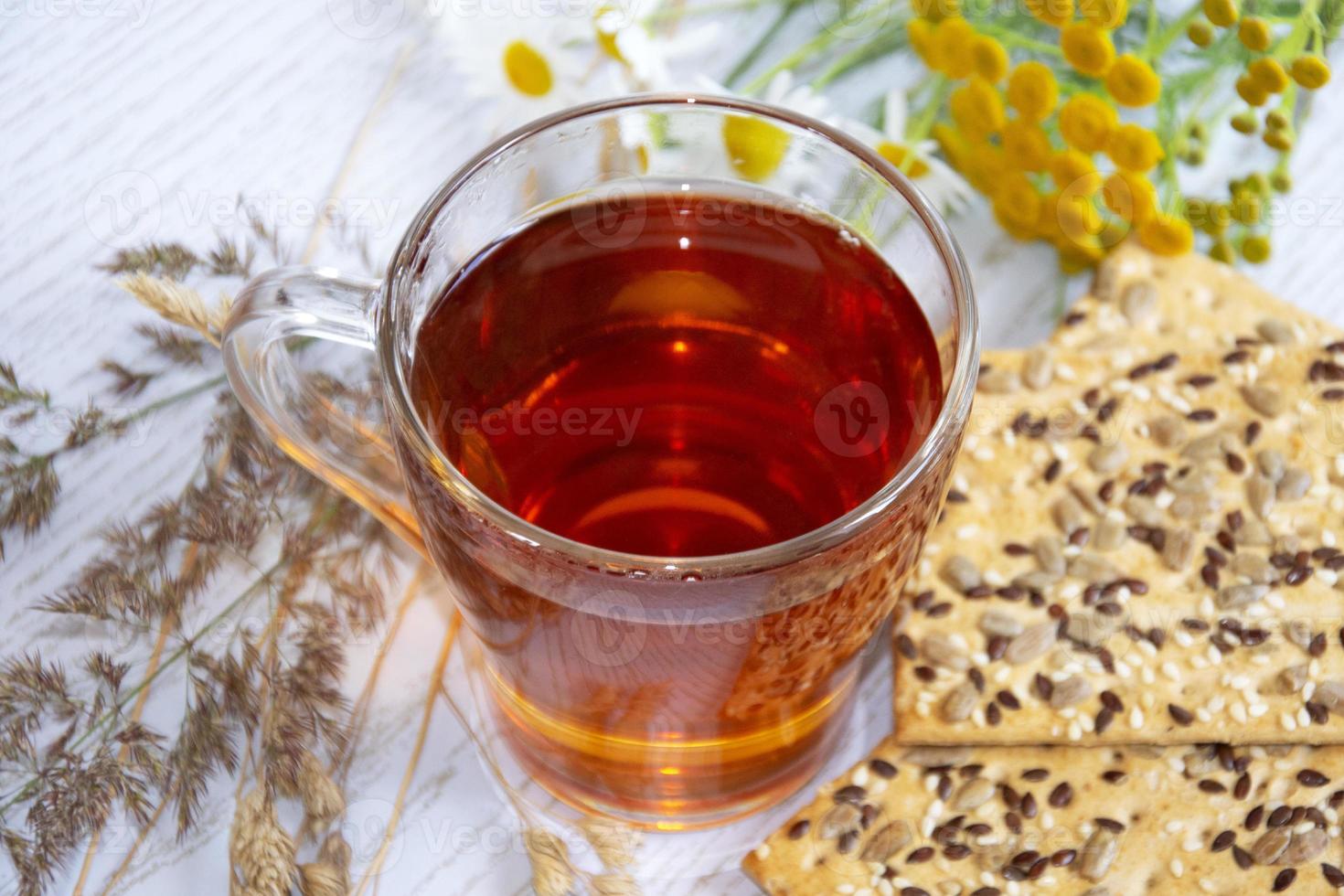 té con galletas. taza de vidrio con té caliente, galletas y flores silvestres. foto