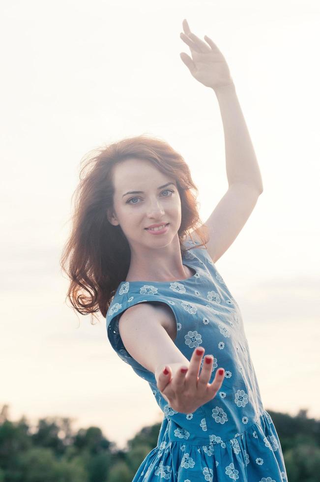 Close up portrait of young beautiful ginger haired woman, dancing, blue eyes and clothes, sunset light, summer, outdoor, motion blur, messy hair by the wind. Street fashion. Freedom concept photo