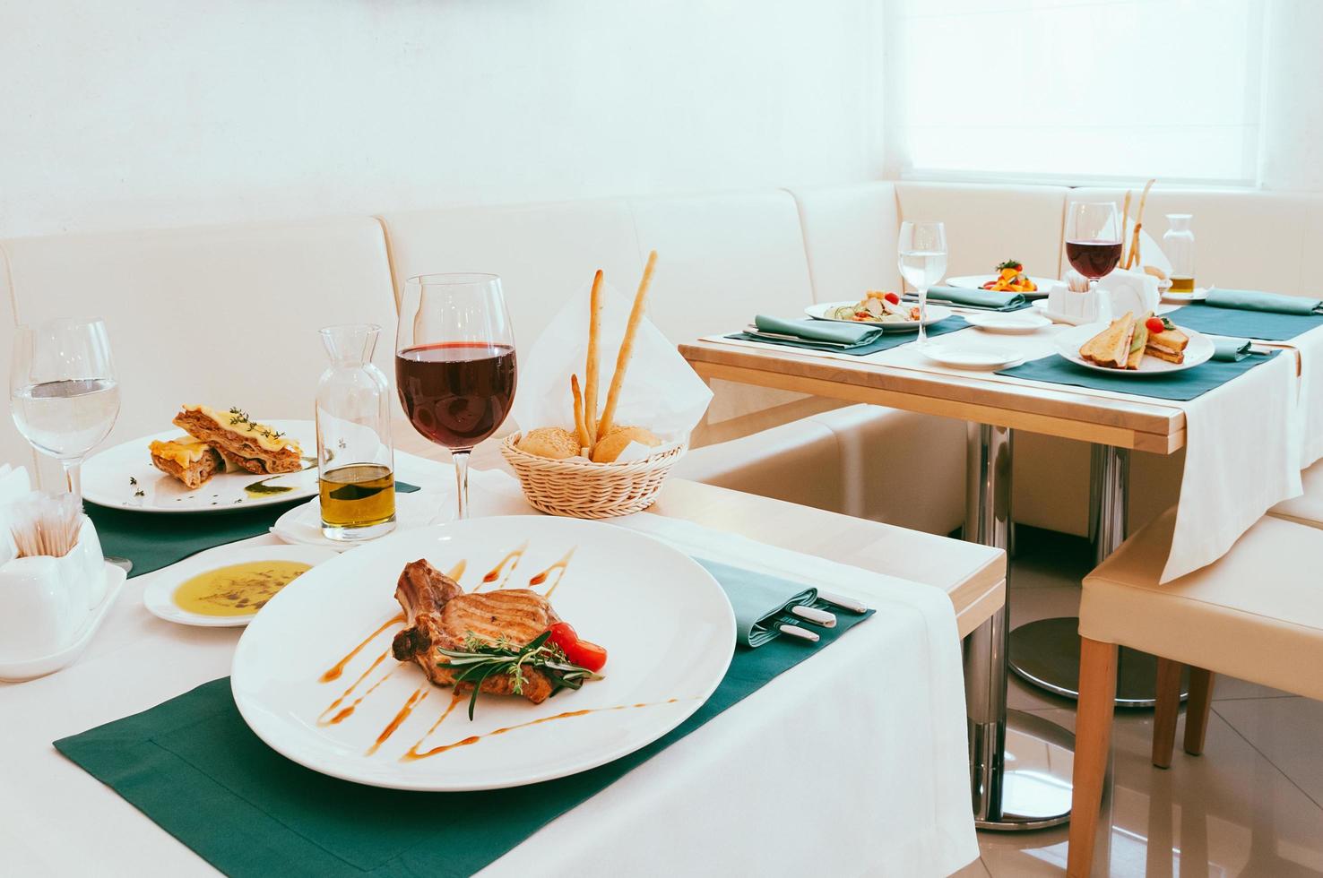 Dining setup with wine and water glasses, cutlery in green napkins, food served on white plates, arranged by catering service in a modern light restaurant, cafe. Italian European cuisine photo