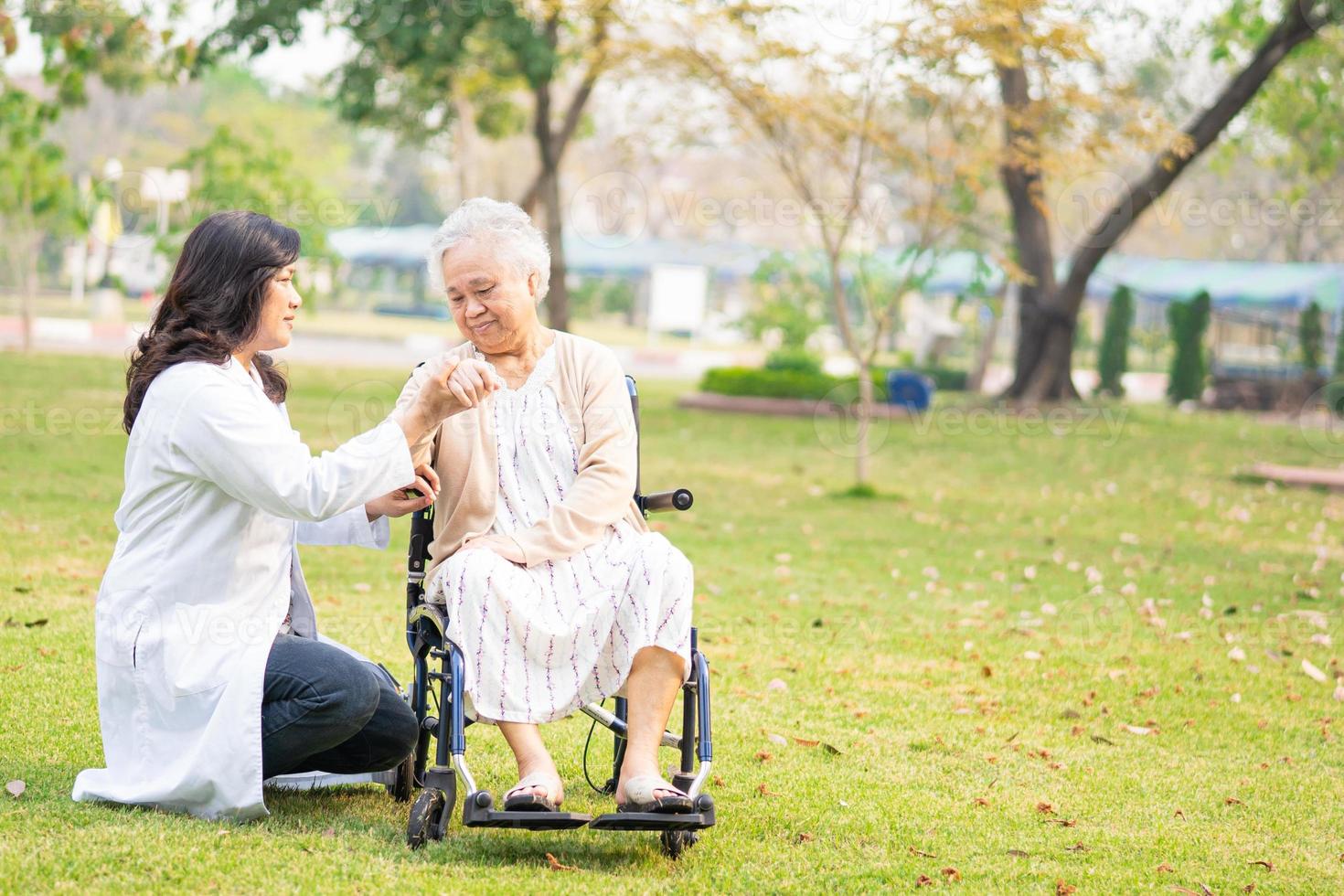 Médico ayuda y atención paciente mujer senior asiática en silla de ruedas en el parque foto