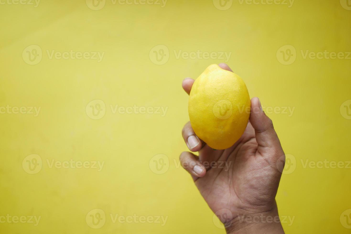 Hand hold Yellow Lemon on yellow background photo