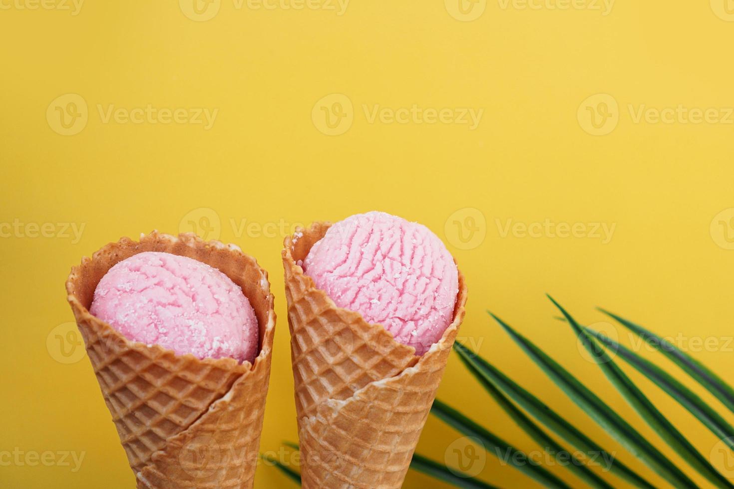 Two strawberry ice creams in a cone on a yellow photo