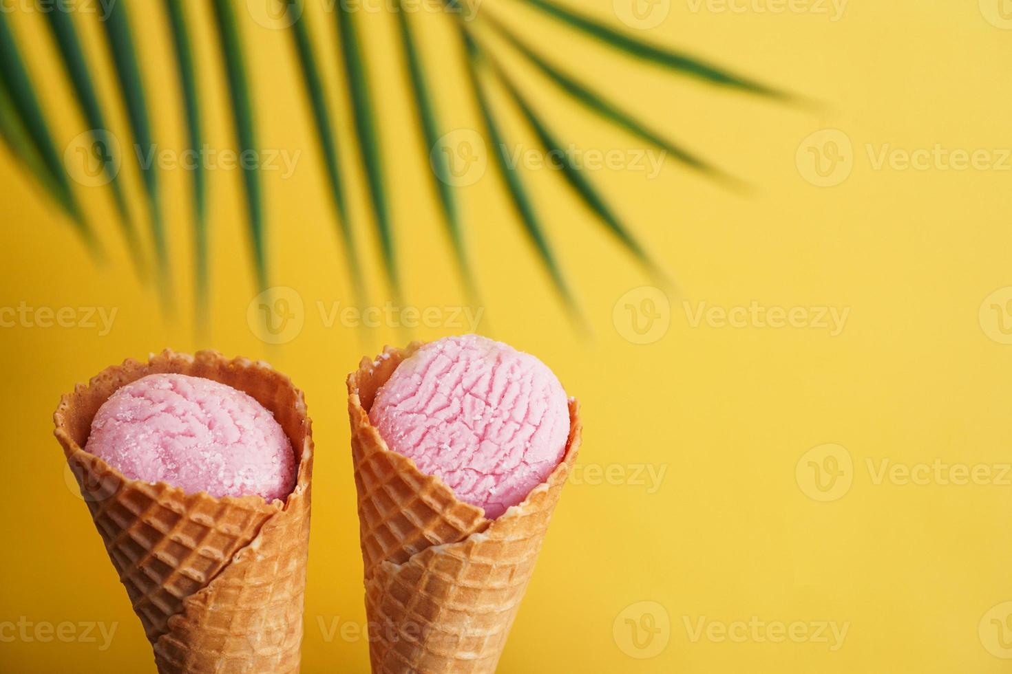 Two strawberry ice creams in a cone on a yellow photo