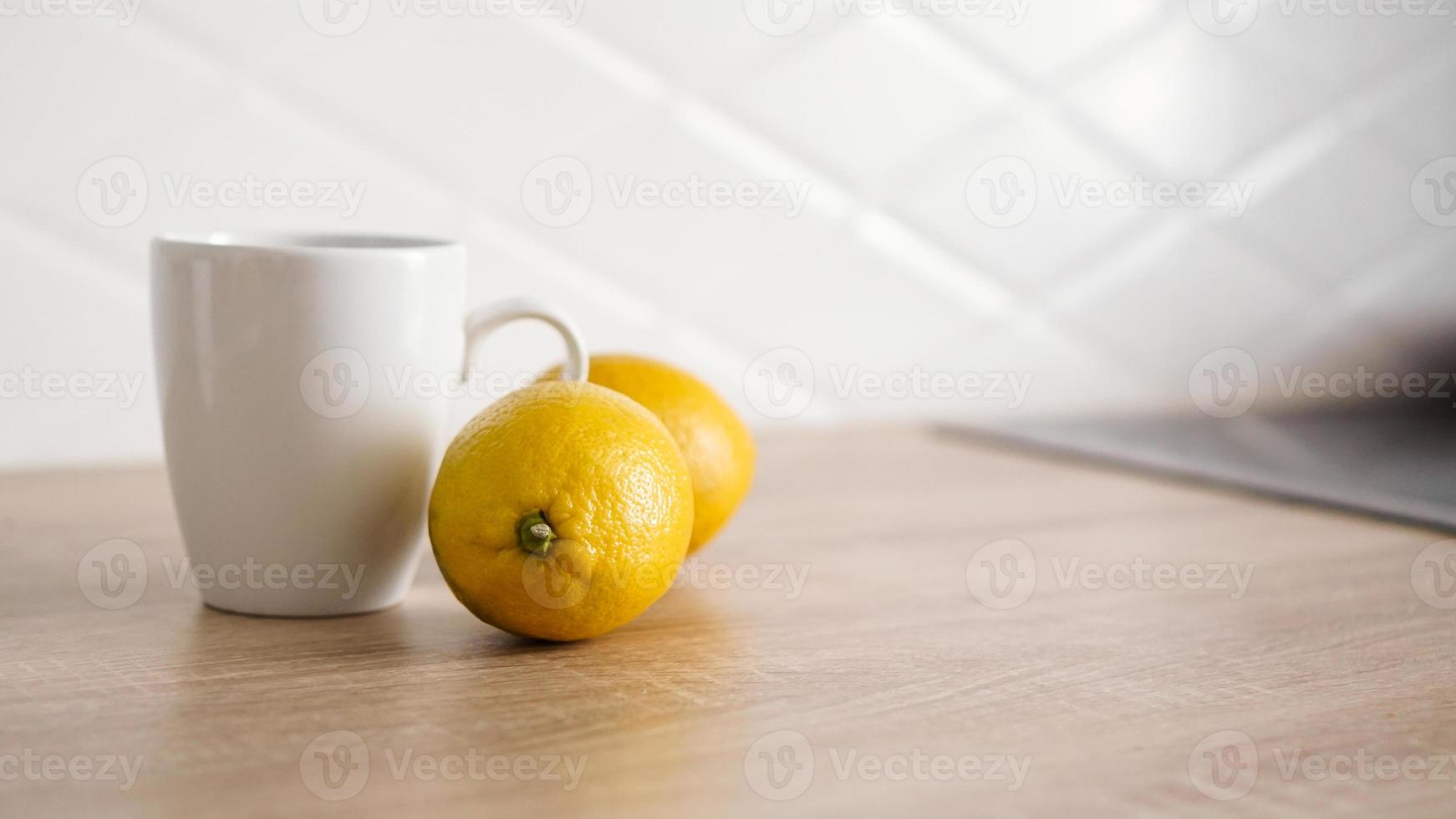 Two lemons on the kitchen table near a white mug of tea photo