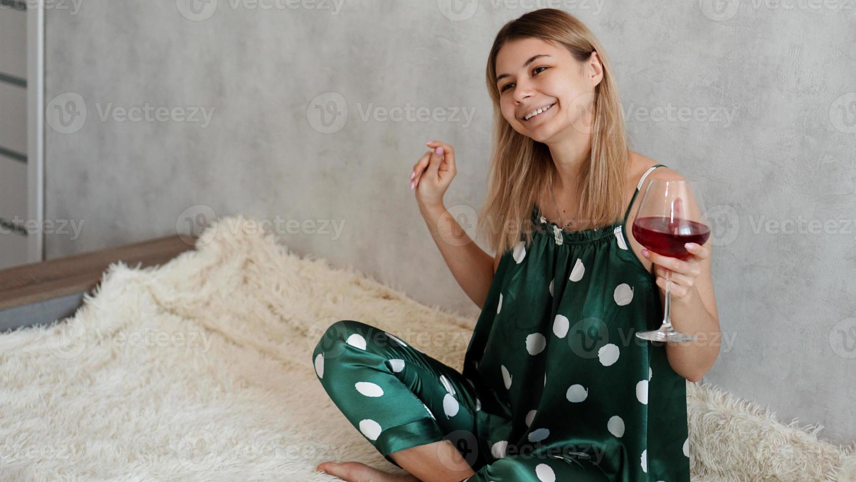 chica en pijama verde en la cama con una copa de vino tinto foto