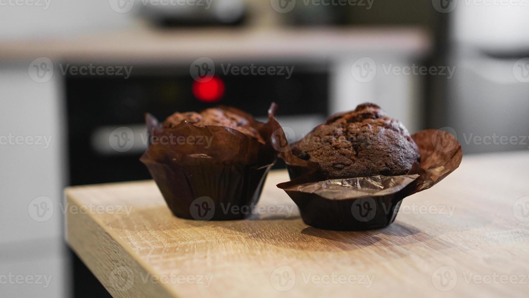 Dos muffins de chocolate sobre una mesa de madera contra la cocina moderna foto