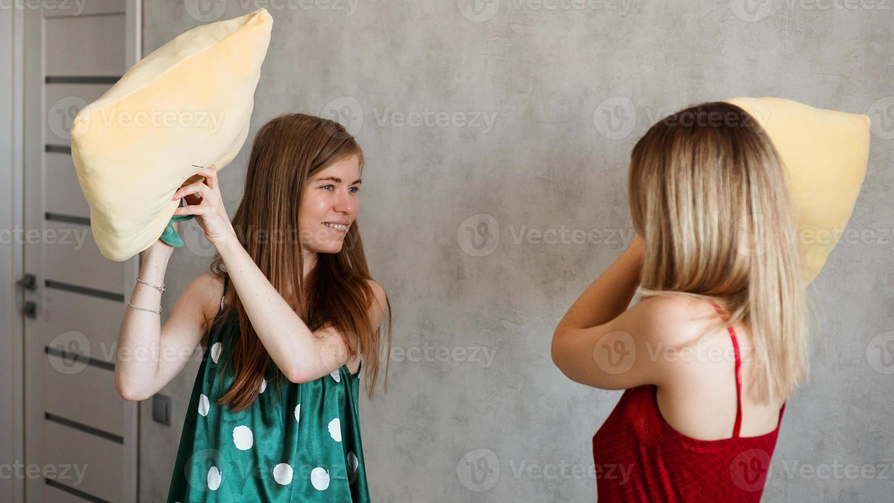 Two girl friends pillow fight in room photo