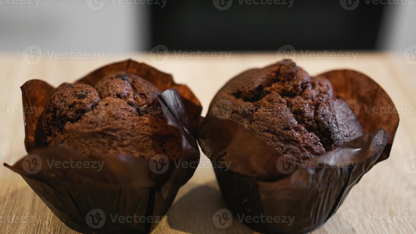 Dos muffins de chocolate sobre una mesa de madera contra la cocina moderna foto
