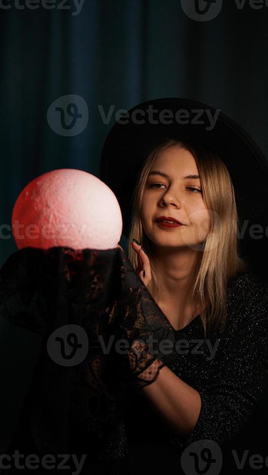 una adivina joven con un sombrero sostiene una bola mágica. foto