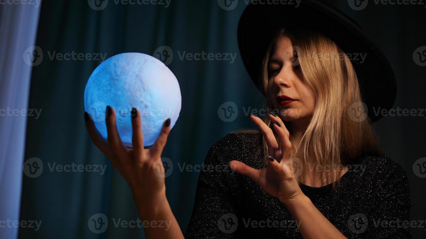 una adivina joven con un sombrero sostiene una bola mágica. foto