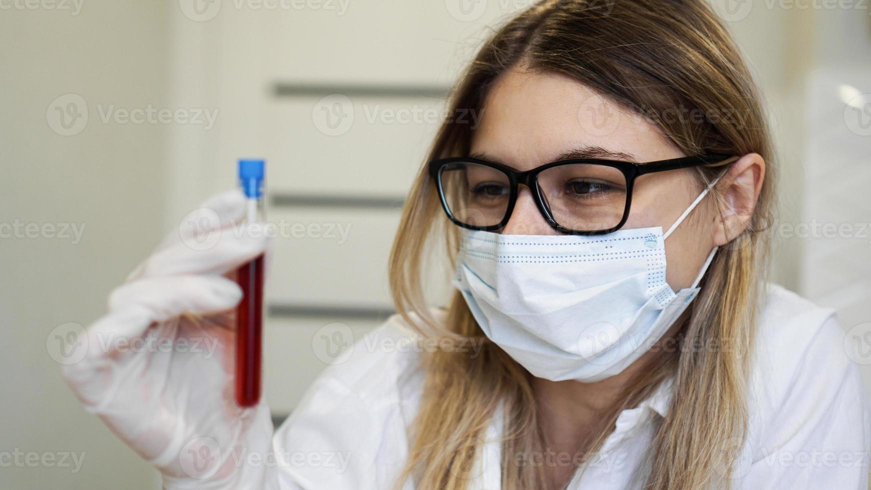 Cerca de la joven científica sosteniendo el tubo de ensayo con muestra de sangre foto