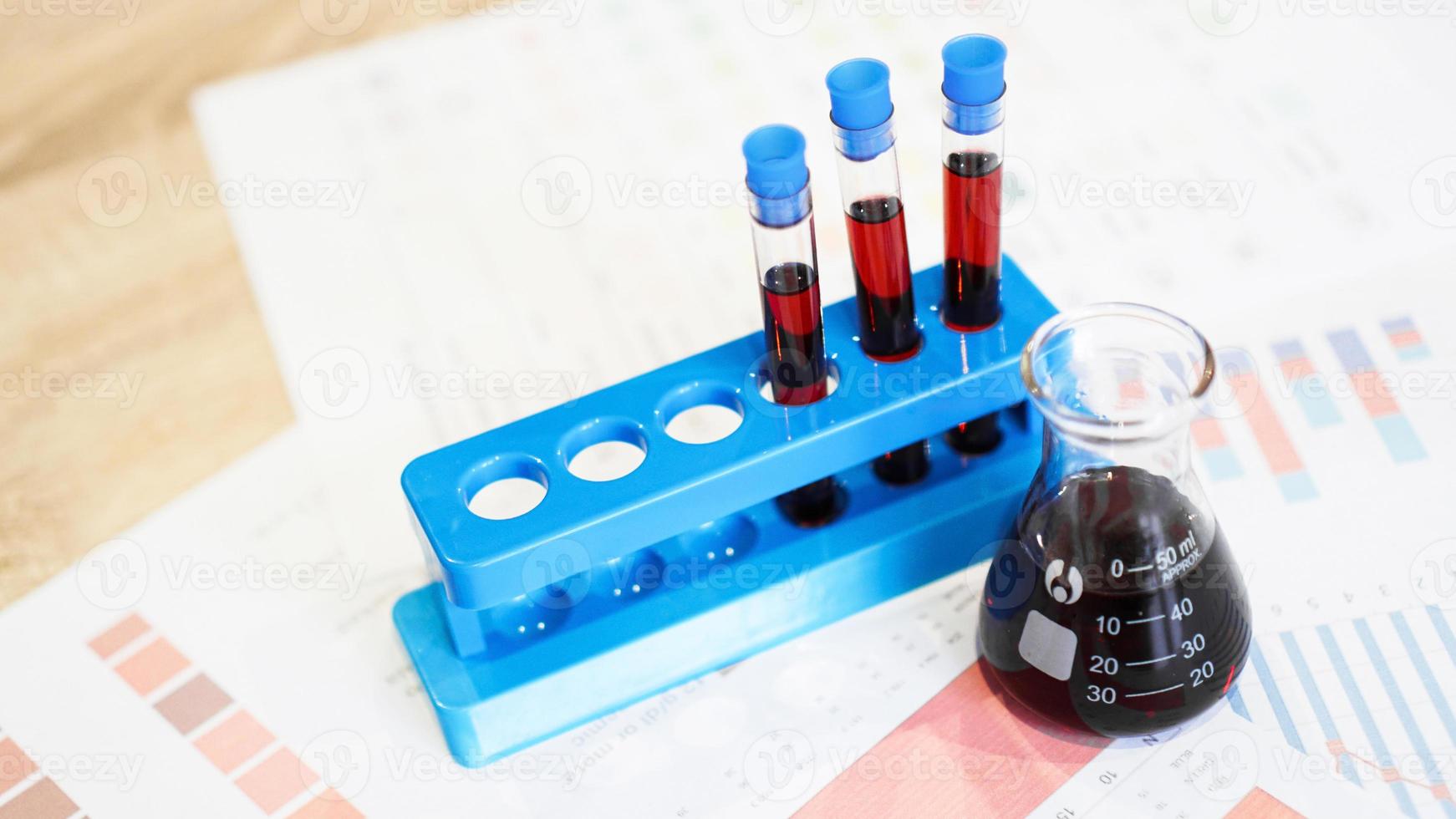 Test tubes on a stand and a flask with red blood on medical documents photo